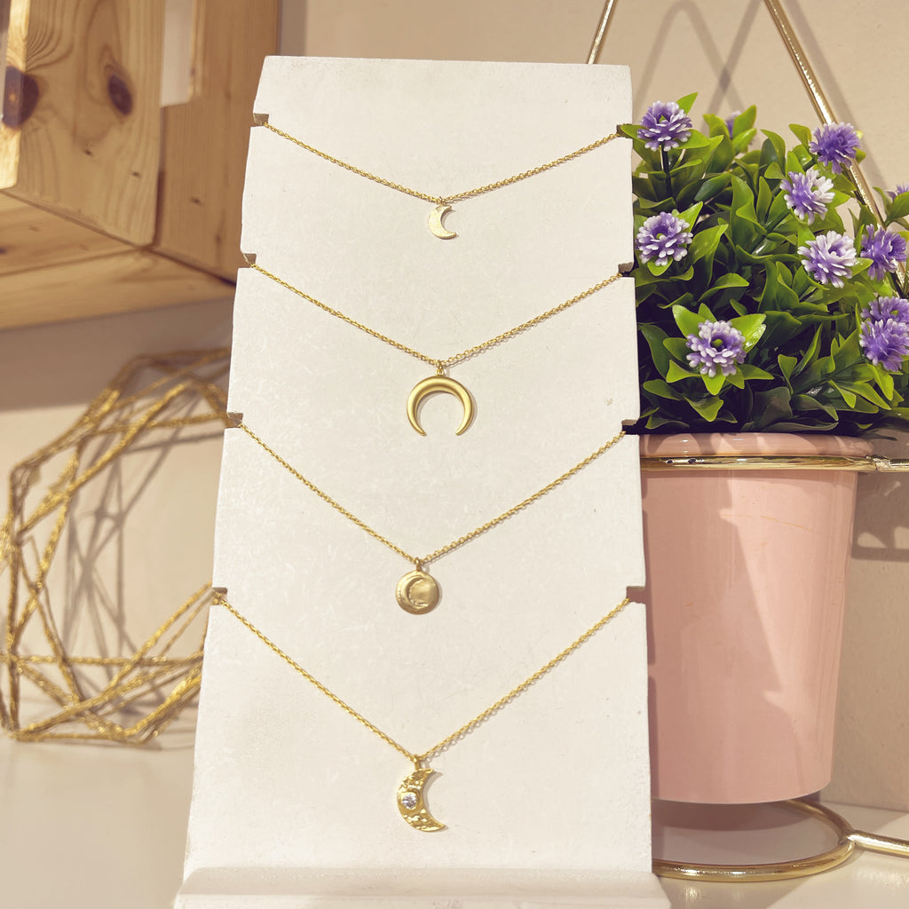 Collar medallita luna dorada junto a otros collares de luna en expositor blanco