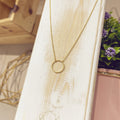 Collar arito dorado sobre expositor blanco con flores de fondo