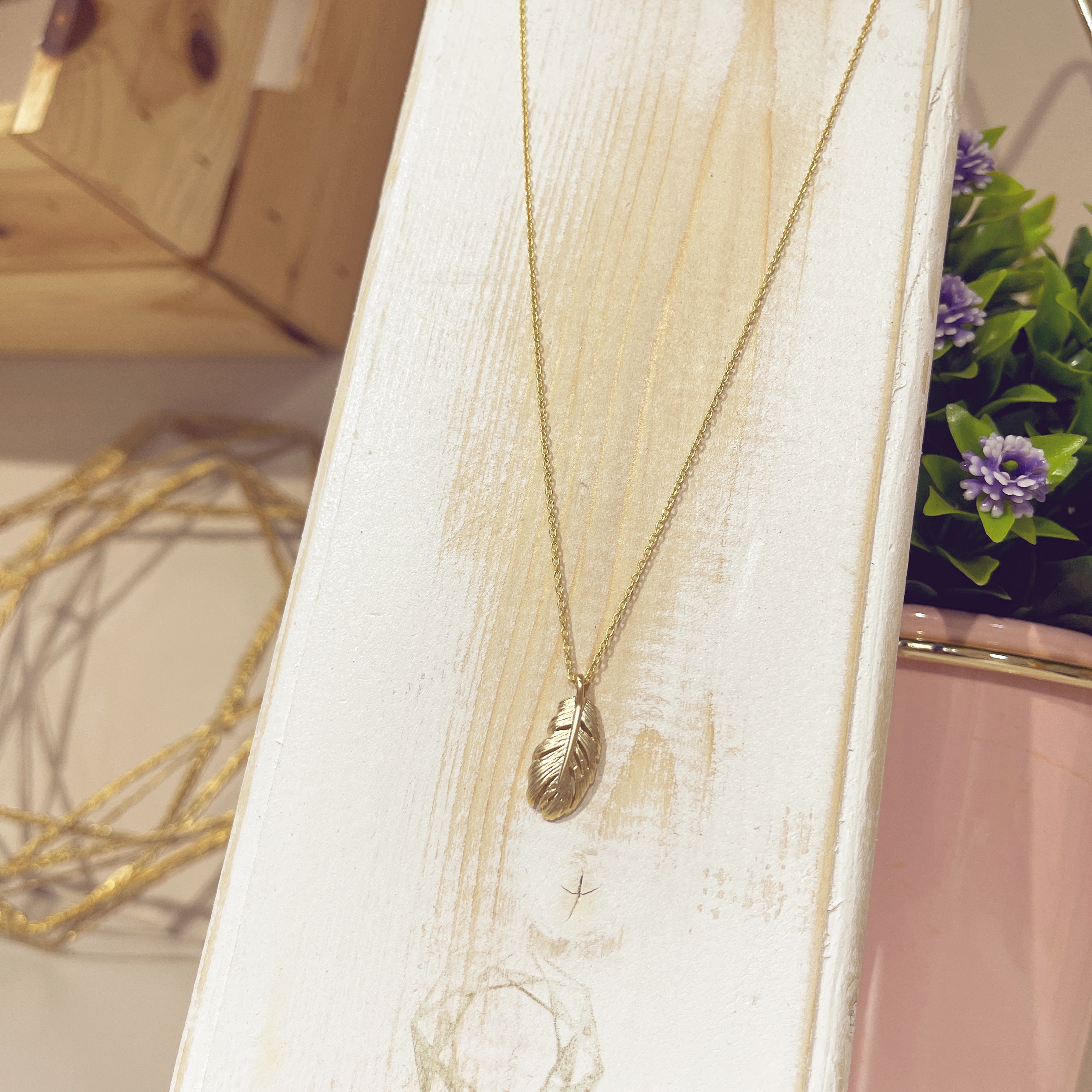 Collar Pluma Real dorada en relieve en expositor blanco