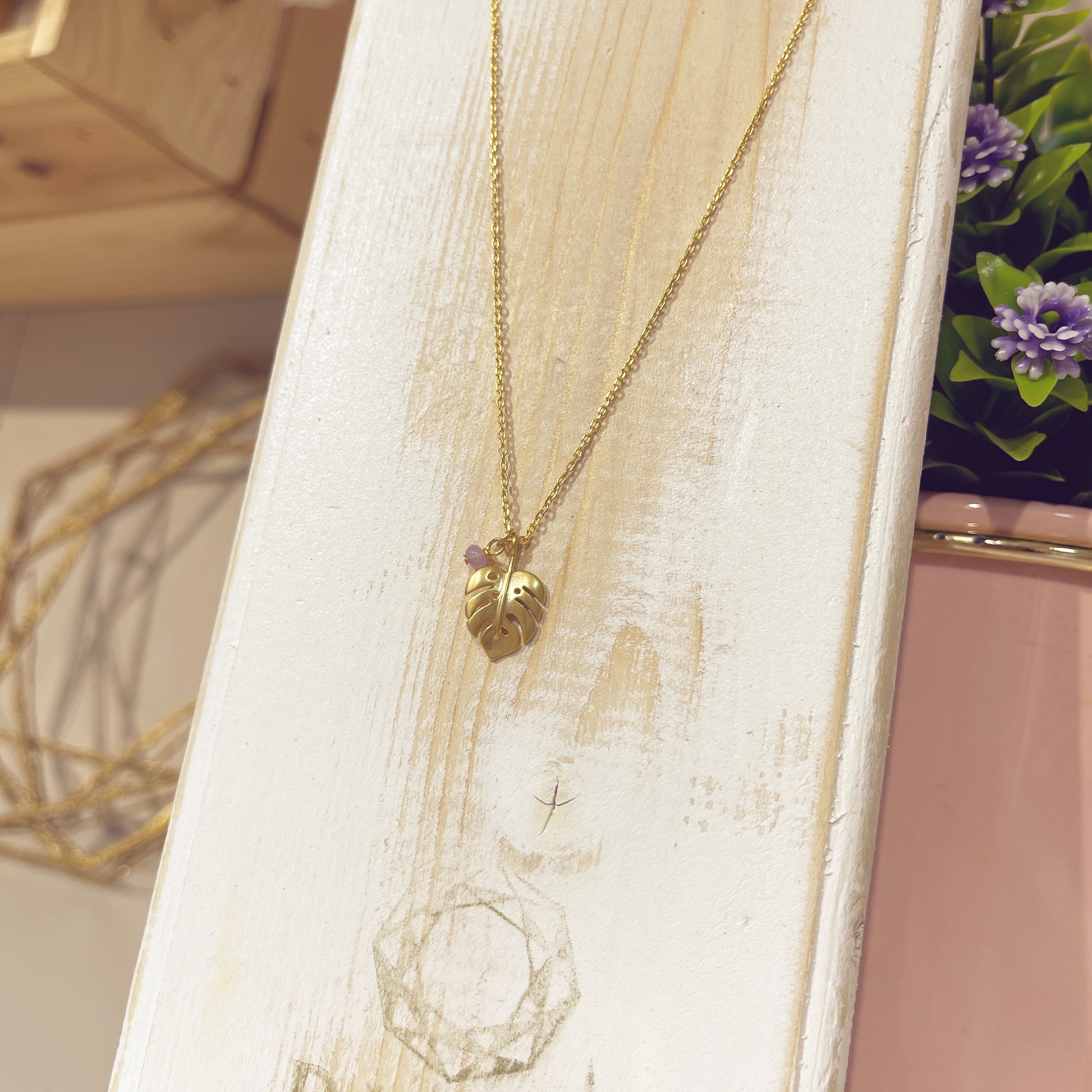 Collar Monstera Mini dorado con piedra lila en expositor blanco