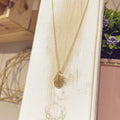 Collar Hoja Palma dorada con textura grabada en expositor blanco