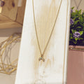 Collar lunita turquesa dorado sobre expositor blanco con flores de fondo