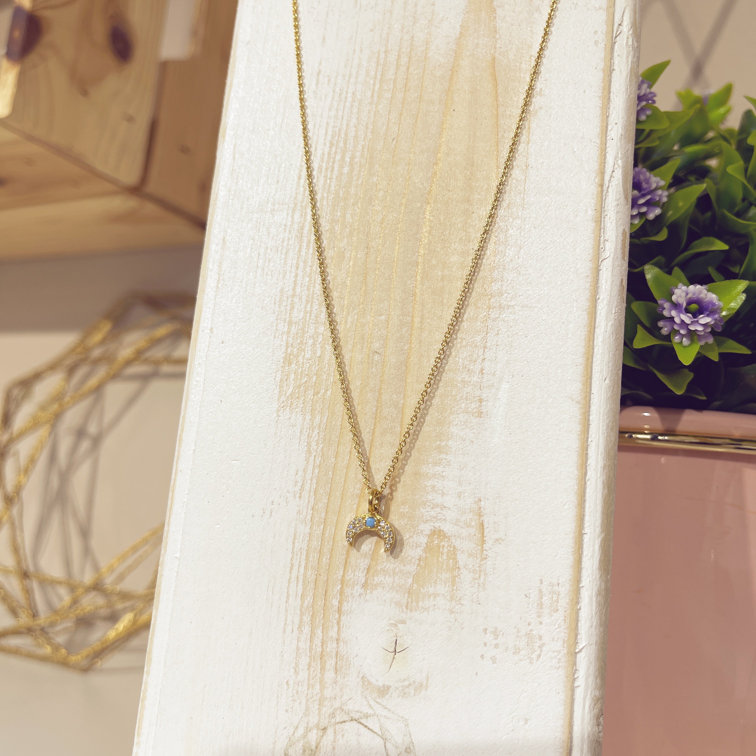 Collar lunita turquesa dorado sobre expositor blanco con flores de fondo