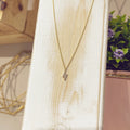 Collar rayo circonitas dorado sobre expositor blanco, vista frontal