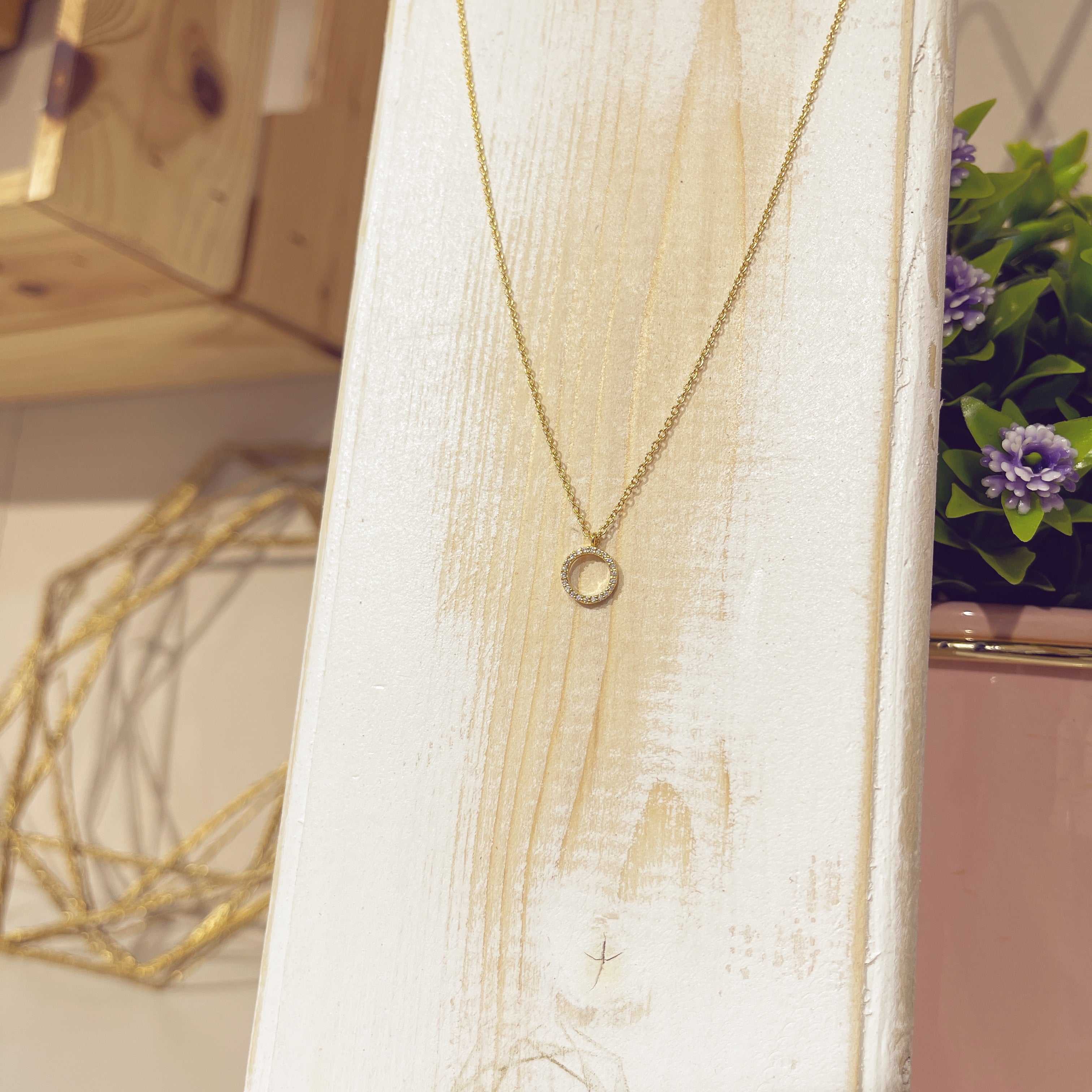 Collar mini arito circonitas dorado sobre expositor blanco con flores de fondo
