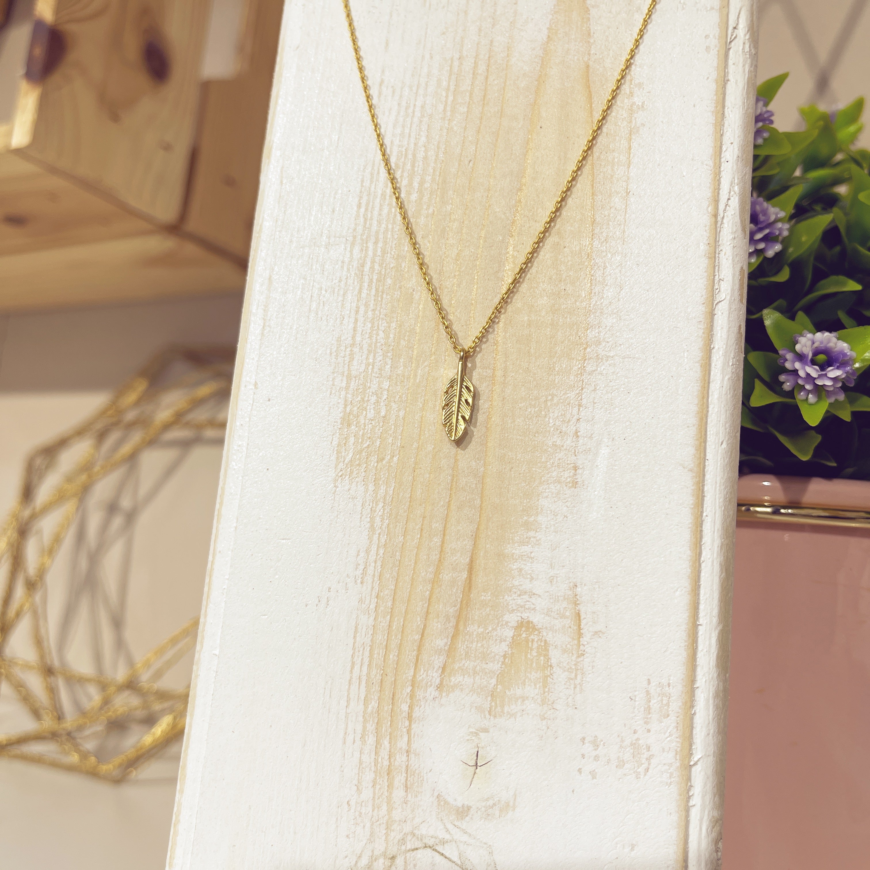 Collar Pluma Mini dorada en relieve en expositor blanco