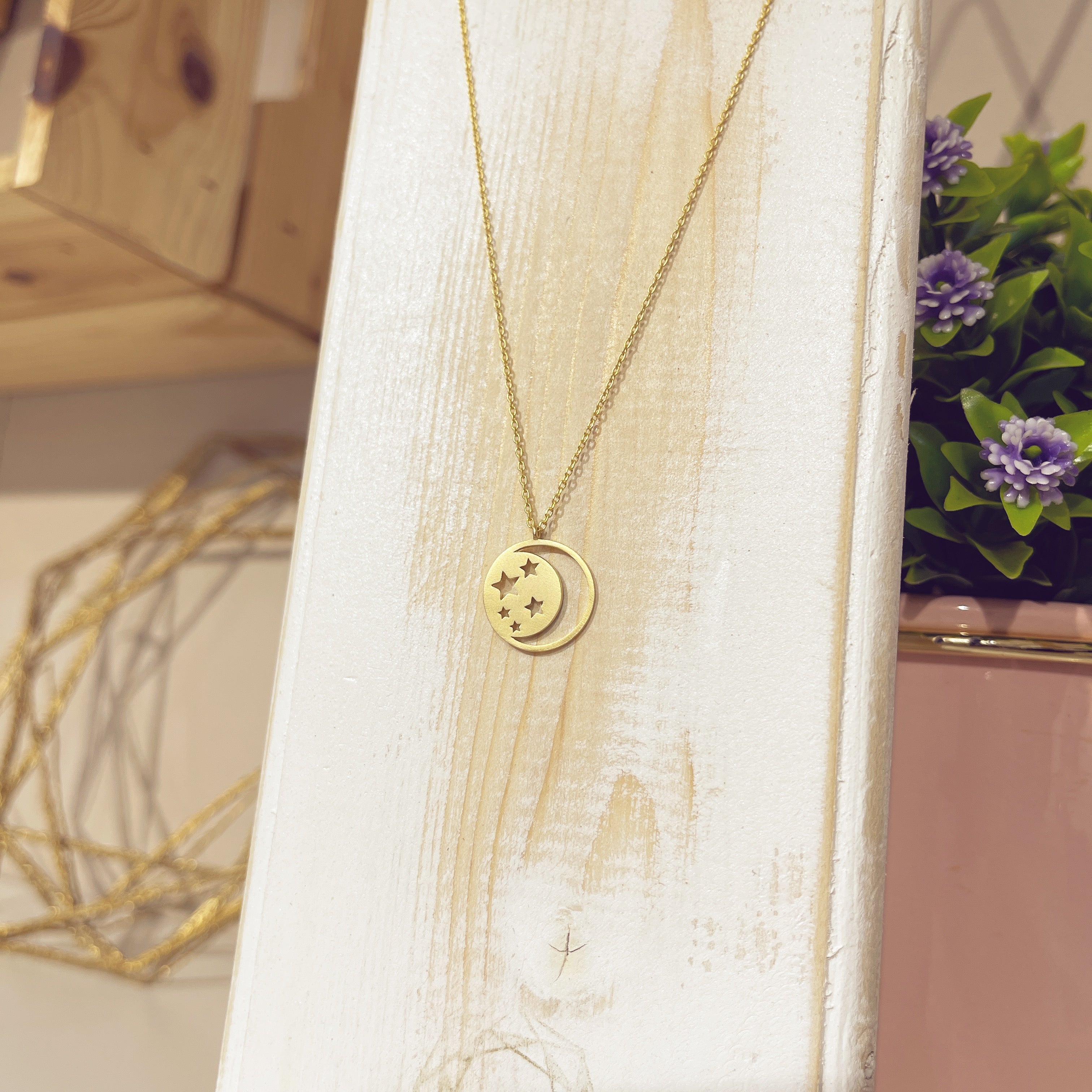 Collar sueño celestial dorado con medallita de luna y estrellas sobre expositor blanco