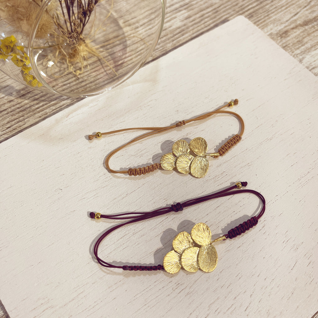 Pulsera Racimo macramé dorada en beis y burdeos sobre superficie blanca