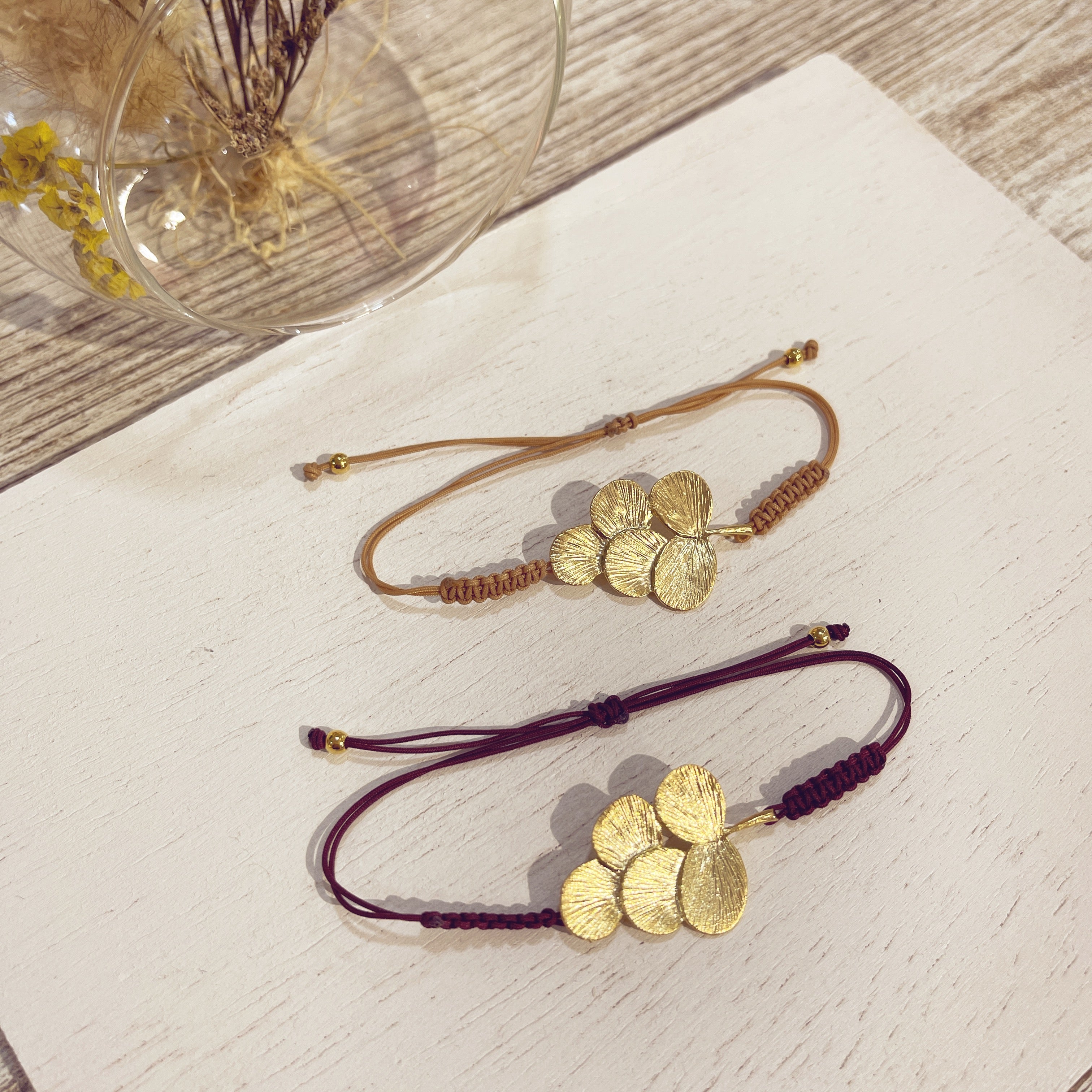 Pulsera Racimo macramé dorada en beis y burdeos sobre superficie blanca