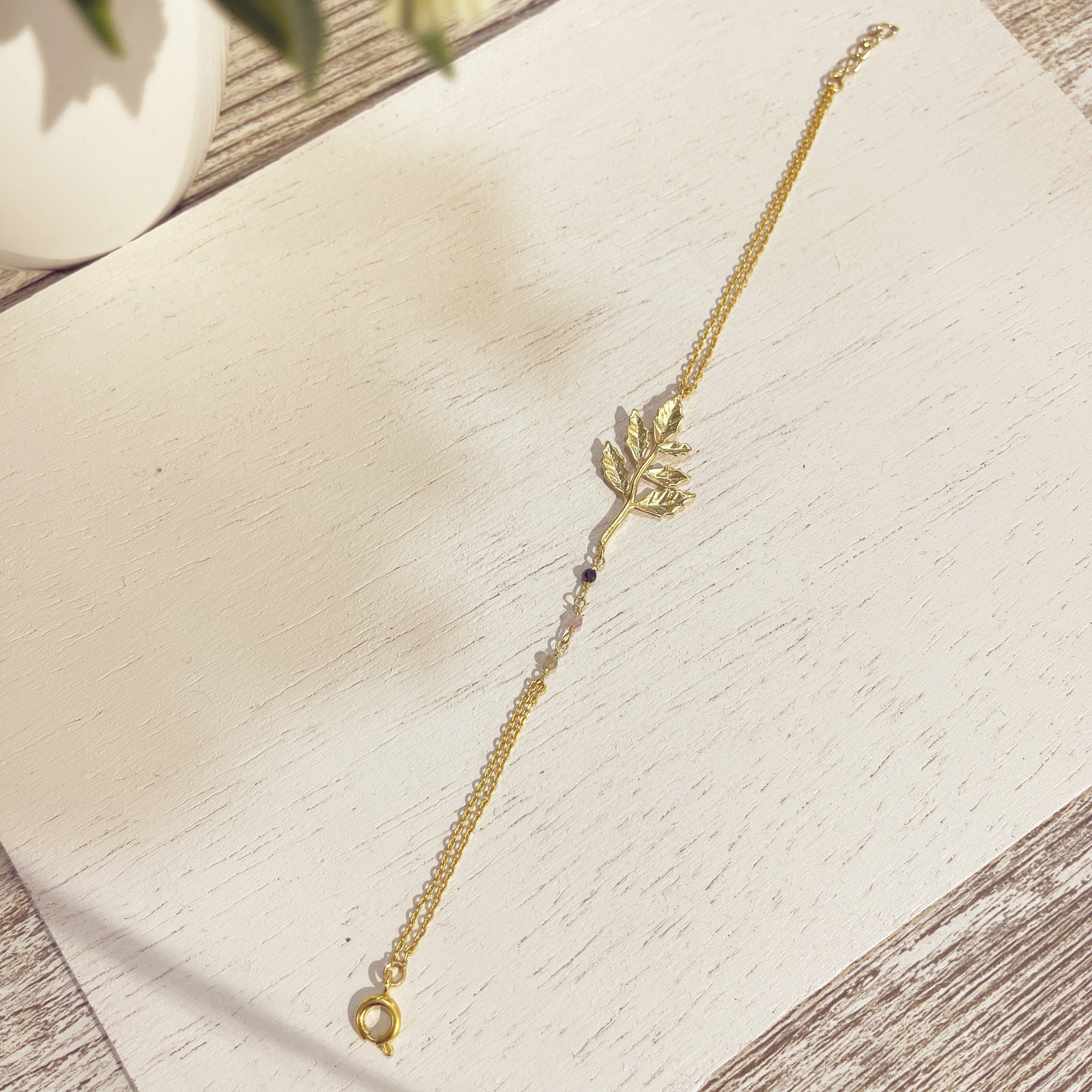 Pulsera Hoja Minera dorada doble cadena con piedrecitas sobre superficie blanca