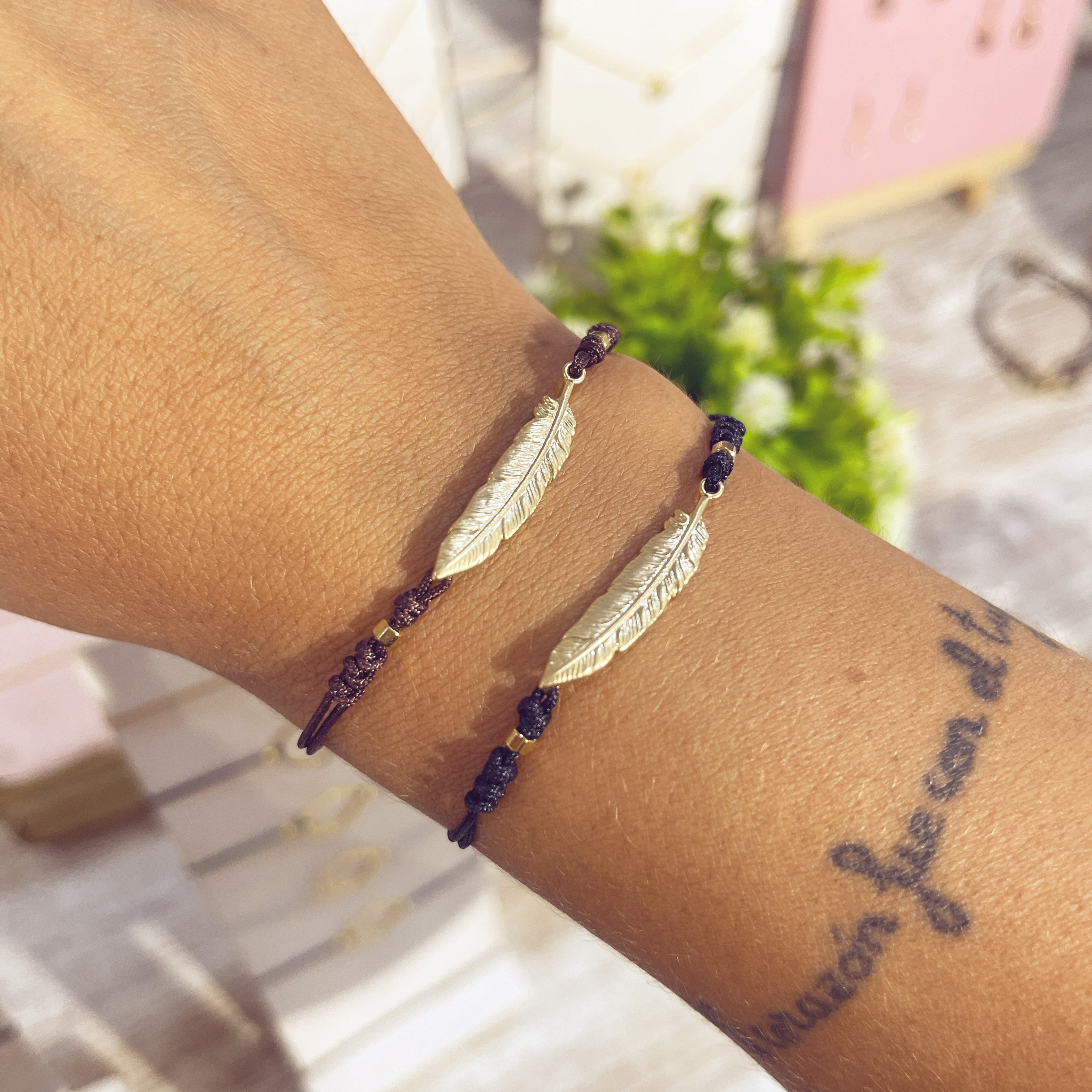 Pulseras Pluma Real doradas en cordón negro en muñeca